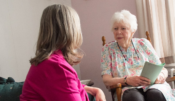 older-woman-holding-papers-in-rocking-chair-talking-to-a-younger-women older woman in rocking chair talking to a younger women