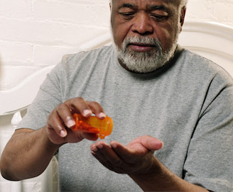 elderly man pouring pills from a pill bottle in to his hand