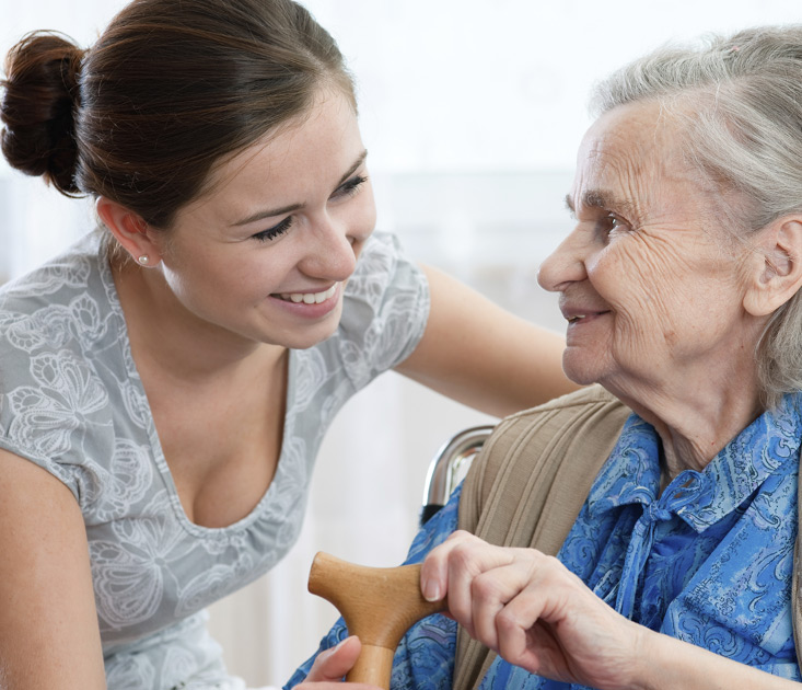 young-woman-smiling-and-conversing-with-elderly-woman-holding-a-cane young woman smiling and conversing with elderly woman holding a cane